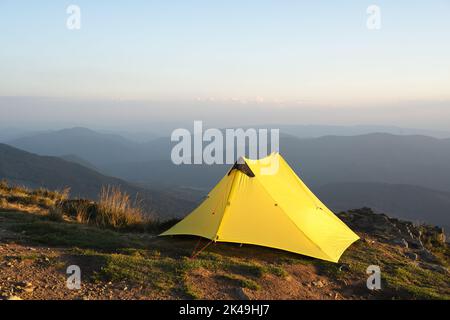Gelbes Zelt vor der Kulisse einer unglaublichen Berglandschaft während des Morgensonnenaufgangs. Unglaubliches Hochland. Tourismuskonzept Stockfoto