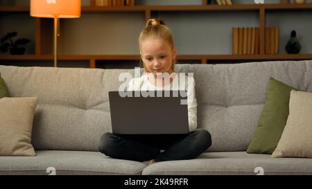 Süßes kleines Gamer-Schulmädchen, das moderne Online-Computerspiele spielt und auf dem Laptop in sozialen Netzwerken chattende Nachrichten auf Spielebene vervollständigt Stockfoto