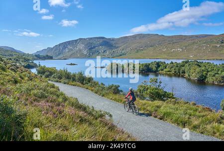 Nette ältere Frau auf dem Mountainbike, Radfahren im Lough Beagh im Glenveagh Nationalpark, in der Nähe von Churchill, Donegal, Nordrepublik Irland Stockfoto