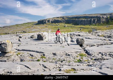 Nette ältere Frau auf dem Mountainbike, mit dem Fahrrad in der rauen Karstlandschaft von Burren in der Nähe von Ballyvaughan, Grafschaft Clare im Westen der Republik Stockfoto