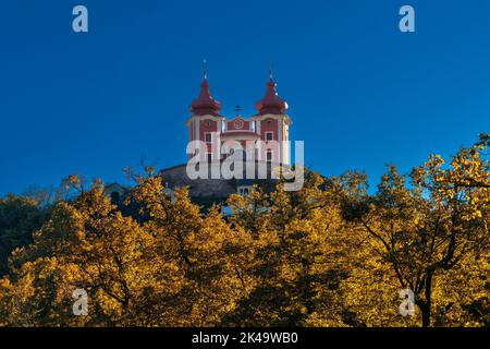 Banska Stiavnica, Slowakei - 28. September 2022: Blick auf den roten Kalvarienberg Banska Stiavnica unter blauem Himmel mit Herbstwald im Vordergrund Stockfoto