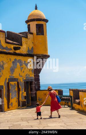 Eine vertikale Aufnahme einer Mutter und eines Sohnes in der Nähe des alten Wachturms in Forte de Sao Tiago, Funchal, Madeira Stockfoto