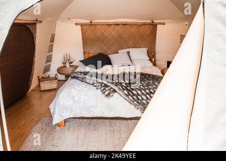 Gemütliches großes Bett im Zeltinneren mit Holzboden und grauen Teppichdecken Kissen und runden Nachttischen, tarawera See, Neuseeland Stockfoto