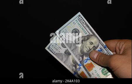 Rechte Hand hält Stapel von zwei 100-Dollar-Banknoten auf schwarzem Hintergrund wird die zwei 100-Dollar-Banknote per Hand übertragen Stockfoto