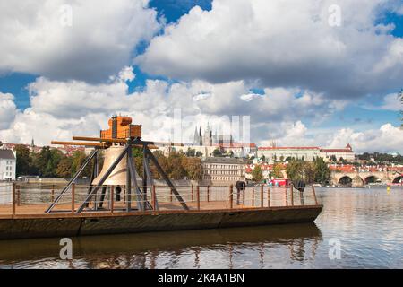 Die Gedenkglocke #9801 auf einem Ponton in der Moldau bei Smetanovo nábřeží. Prag. Prager Burg und Karlsbrücke im Hintergrund. Stockfoto