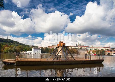 Die Gedenkglocke #9801 auf einem Ponton in der Moldau bei Smetanovo nábřeží. Prag. Prager Burg und Karlsbrücke im Hintergrund. Stockfoto