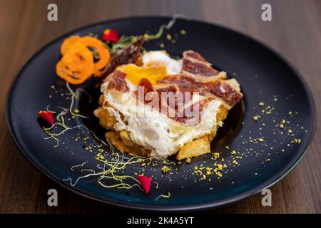 Eine Nahaufnahme von köstlichen Huevos rotos. Ein spanisches Gericht mit Spiegeleiern, Kartoffeln und Fleisch. Stockfoto