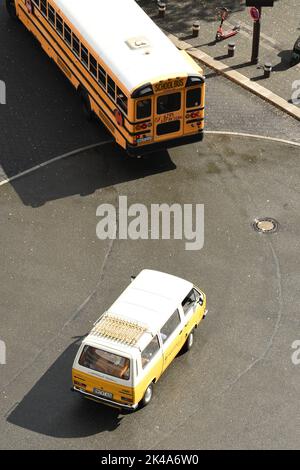 Eine vertikale Aufnahme eines gelb-weißen Automobils, das auf einer Straße hinter einem amerikanischen Schulbus fährt Stockfoto