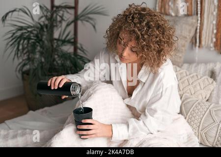 Weibchen gießt Wasser in den Becher auf dem Bett Stockfoto