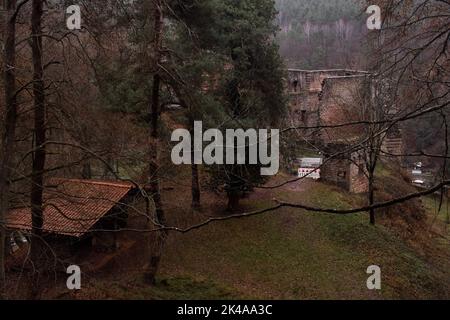 Frankenstein, Deutschland - 26. Dezember 2020: Kleines Gebäude in den Bäumen mit Burgruine Frankenstein im Hintergrund an einem dunklen Wintertag in deutscher Sprache Stockfoto