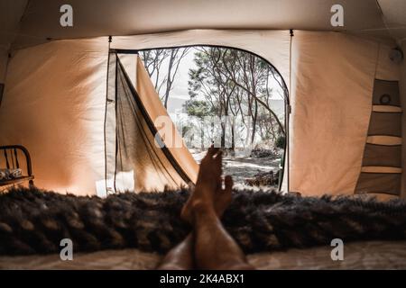 Füße Zehen und Beine einer Person, die ruhig auf dem Bett mit Decke im Zelt im Wald am See, tarawera See, Neuseeland liegt Stockfoto
