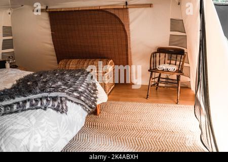 Schönes, komfortables Zimmer in einem Zelt mit einem großen Korbkoffer und einem alten Holztisch mit zwei rollbaren Handtüchern Stockfoto