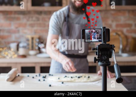 Videorezept. Gefällt Feedback. Virtuelles Kochtraining. Blaubeerkuchen. Chefkoch Blogger Aufnahme Live-Streaming auf Smartphone auf Stativ in unfokussed Stockfoto