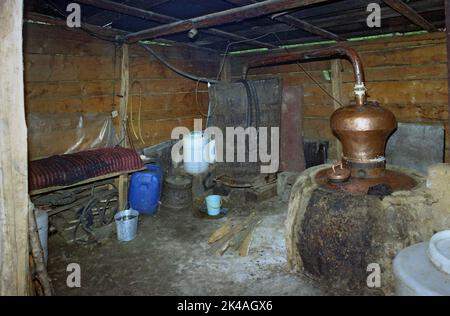 Zubereitung von hausgemachtem Pflaumenbrand (Tuica) auf dem Land Rumäniens. Destillation in einem Kupfer noch über einem Ofen. Stockfoto