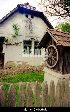 Arad County, Rumänien, ca. 2000. Altmodischer Wasserbrunnen auf einem privaten Grundstück mit einem jahrhundertealten traditionellen Haus. Stockfoto