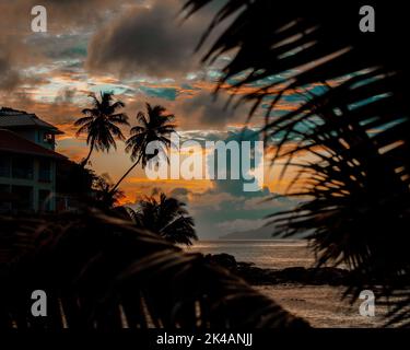 Eine wunderschöne tropische Landschaft mit Silhouetten von Palmen am Meer unter einem bunten Himmel bei Sonnenuntergang Stockfoto