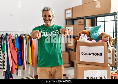 Mittelalter hispanischer Mann trägt Freiwillige T-Shirt bei Spenden Stand zeigt auf Sie und die Kamera mit den Fingern, lächelnd positiv und fröhlich Stockfoto