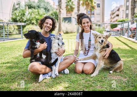 Mann und Frau Paar lächeln selbstbewusst auf Kraut mit Hunden im Park sitzen Stockfoto
