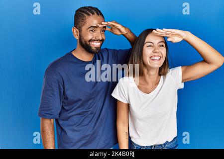 Junge hispanische Paare stehen zusammen sehr glücklich und lächelnd und schauen weit weg mit der Hand über dem Kopf. Suchkonzept. Stockfoto