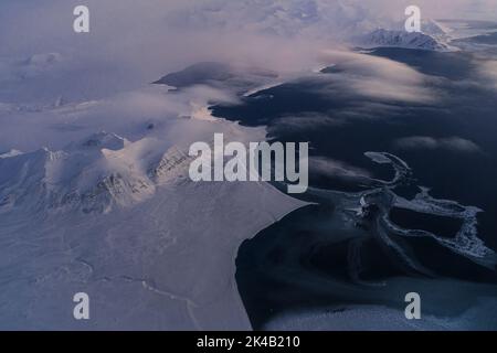 Einzigartige Luftaufnahmen von gefrorenen verschneiten Winterlandschaften der Spitzbergen Berge und Küste, aufgenommen von Flugzeug / Drohne bei Sonnenuntergang Stockfoto