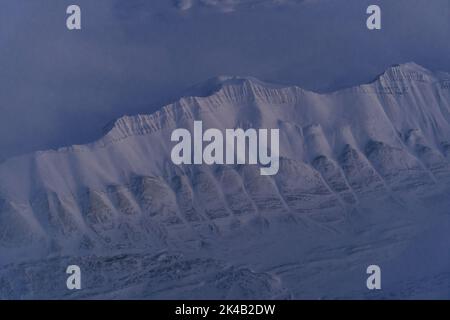 Einzigartige Luftaufnahmen von gefrorenen verschneiten Winterlandschaften der Spitzbergen Berge und Küste, aufgenommen von Flugzeug / Drohne bei Sonnenuntergang Stockfoto