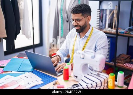 Junger arabischer Mann, der im Schneidergeschäft mit einem Laptop lächelnd zulächelt Stockfoto