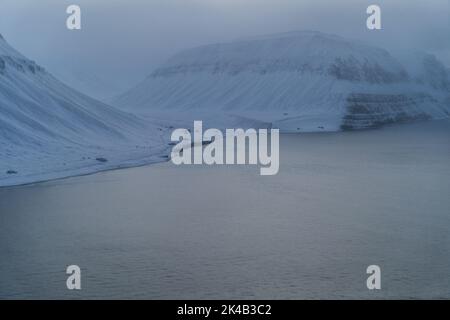 Einzigartige Luftaufnahmen von gefrorenen verschneiten Winterlandschaften der Spitzbergen Berge und Küste, aufgenommen von Flugzeug / Drohne bei Sonnenuntergang Stockfoto