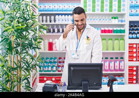 Junger hispanic-Mann Apotheker im Gespräch auf Smartphone mit Computer in der Apotheke Stockfoto