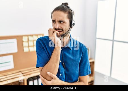 Junger hispanischer Mann mit Bart, der im Büro ein Callcenter-Agenten-Headset trägt, gestresst und nervös aussieht, mit Händen auf dem Mund, beißende Nägel. Angst p Stockfoto
