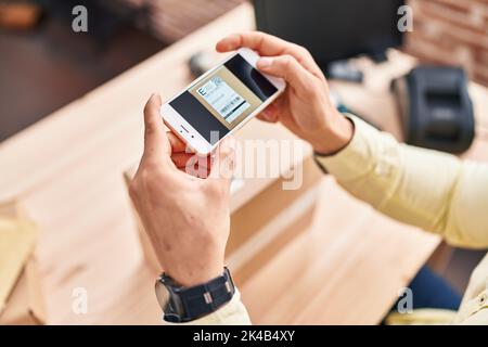 Junger hispanischer Mann E-Commerce-Business-Mitarbeiter Scannen Etikett mit Smartphone im Büro Stockfoto