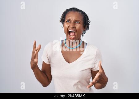 Afrikanische Frau mit Dreadlocks stehen über weißem Hintergrund verrückt und verrückt Schreien und Schreien mit aggressivem Ausdruck und Arme angehoben. Frustration Stockfoto