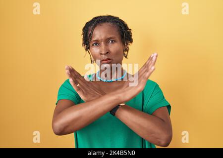 Afrikanische Frau mit Dreadlocks stehen über gelben Hintergrund Ablehnung Ausdruck Kreuzung Arme tun negative Zeichen, wütend Gesicht Stockfoto