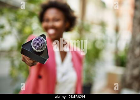 Junge afroamerikanische Journalistin zeigt Reportermikrofon auf die Kamera für Fernsehnachrichten Stockfoto