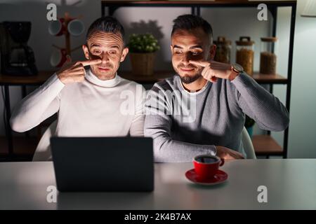 Homosexuelles Paar mit Computer-Laptop zeigt mit der Hand Finger auf Gesicht und Nase, lächelnd fröhlich. Beauty-Konzept Stockfoto