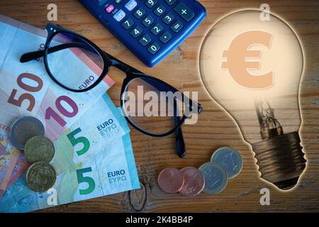 Illustration zum Thema der Kosten der elektrischen Energie, mit Euro-Münzen und Banknoten Rechner und Brille und eine Glühbirne in Transparenz Stockfoto