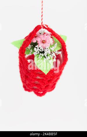 Ein Blumentopf in einem gestrickten Deckel. Es befindet sich auf einem weißen Hintergrund. Nahaufnahme. Stockfoto