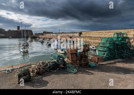 Dunbar Victoria Harbour mit Yachten im Wasser, Hummerkregen und Seilen im Vordergrund und Schloss im Hintergrund bei Sonnenlicht unter dunklem stürmischem Himmel. Stockfoto