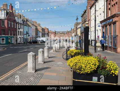 Dunbar High Street mit blühenden Pflanzgefäßen im Vordergrund mit gelben und blauen Adern unter blauem Himmel an einem sonnigen Tag. Stockfoto