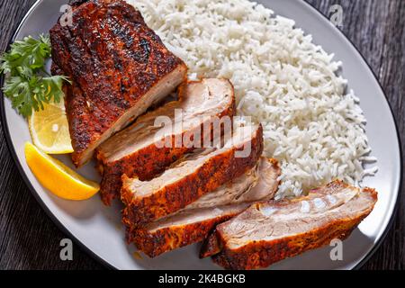 Nahaufnahme der fleischigen Rippen des gebratenen Schweinebackes auf dem Teller mit Basmati-Reis Stockfoto
