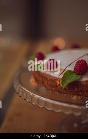 Kuchen mit weißer Glasur, dekoriert mit frischen Himbeeren und Minzblättern auf einem Holztisch in einem Café. Stockfoto