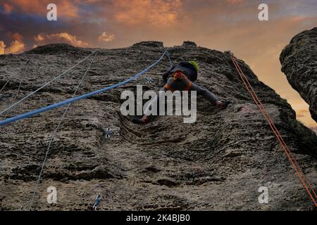 Mann im Helm, der auf einem Felsen klettert. Training für Bergsteiger Stockfoto