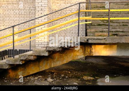 Alte Betontreppen mit gelbem Metallgeländer, die zum Gebäude führen. Stockfoto