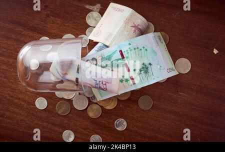 Eine Draufsicht auf kolumbianische Peso-Banknoten und Münzen in gefallener Glasschale auf Holztisch Stockfoto