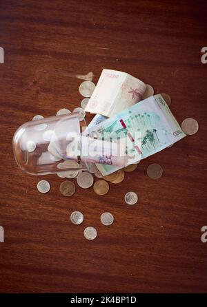 Eine Draufsicht auf kolumbianische Peso-Banknoten und Münzen in gefallener Glasschale auf Holztisch Stockfoto