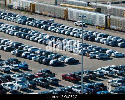 Eine Luftaufnahme eines Autoverteilungs- und Zulassungszentrums, das sich an einem sonnigen Tag neben Güterzugwagen befindet. Stockfoto