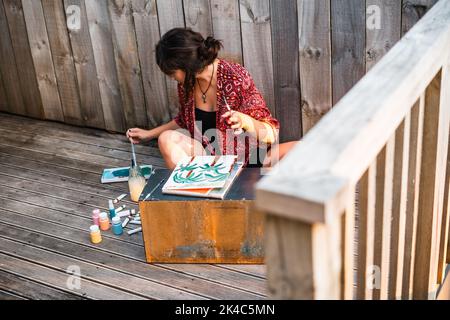 Junge Malerin, die auf dem Boden sitzt und den Pinsel in die Palette taucht Stockfoto