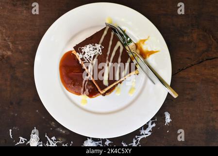 Kokoskuchen auf weißem Teller mit einem Löffel und Karamellsoße Stockfoto