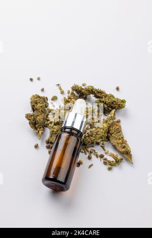 Vertikale Abbildung einer Flasche CBD-Öl und getrockneten Marihuana-Blättern auf weißer Oberfläche Stockfoto