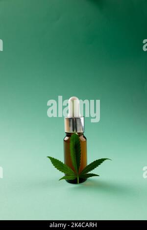 Vertikale Abbildung einer Flasche CBD-Öl und Marihuana-Blatt auf grüner Oberfläche Stockfoto