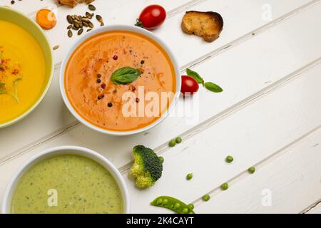 Horizontales Bild von Schüsseln aus Karotten, Brokkoli und Tomatensuppen auf weißem Holz, mit Platz für Kopien Stockfoto